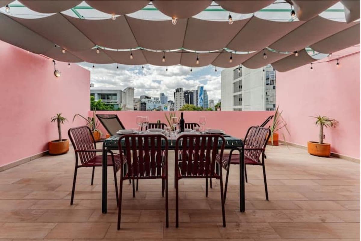 Rooftop dining area with a long table, red chairs, and acoustic ceiling panels.