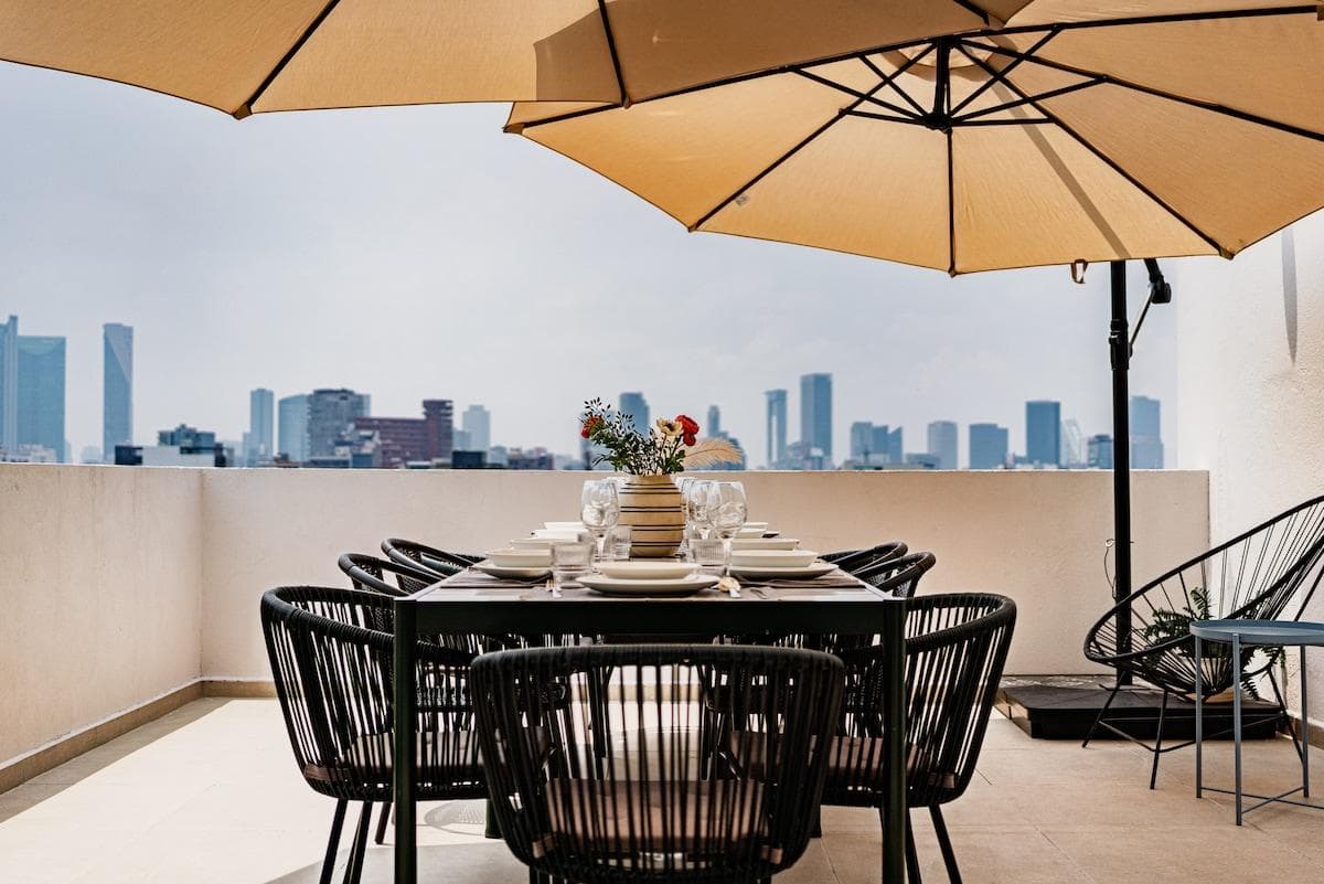 Rooftop dining area shaded by large umbrellas and framed by city views.